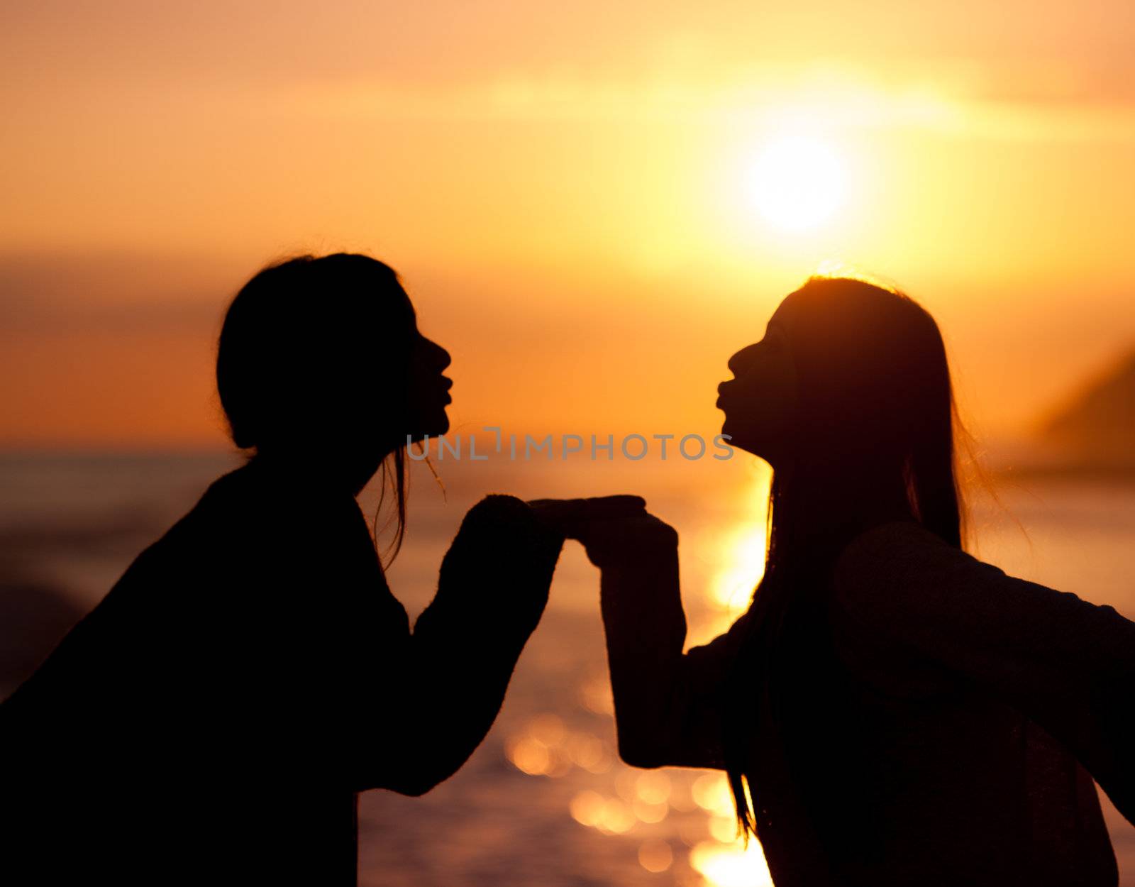 silhouette two young beautiful friends kiss on sunset