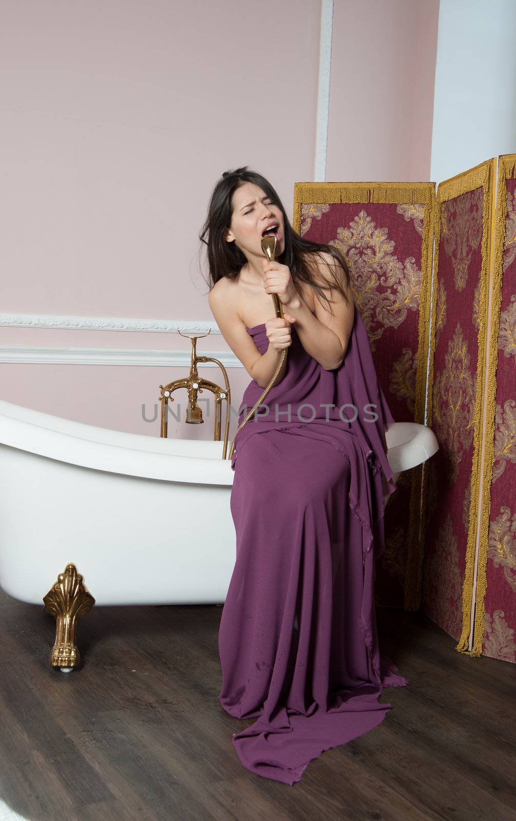 woman in tissue sings in the shower while sitting on the bathtub