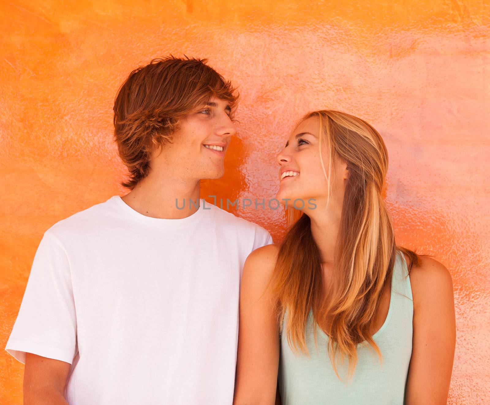 Young beautiful couple having great time over orange background