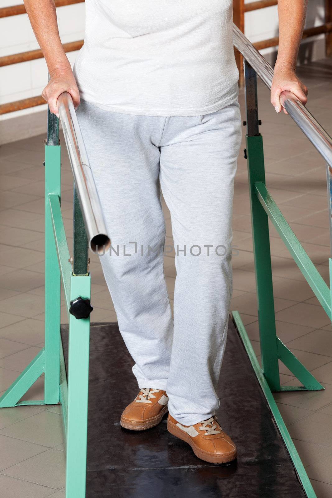 Low section of a senior woman walking with the help of support bars at hospital gym