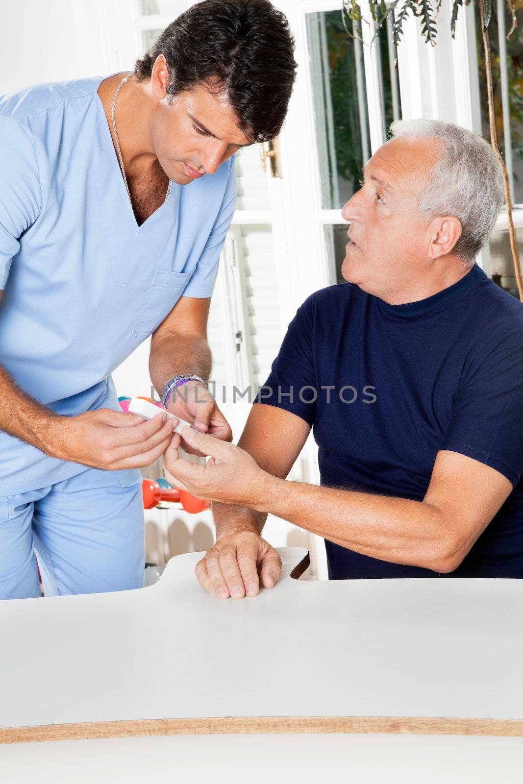 Male nurse checking sugar level of senior man through glucometer