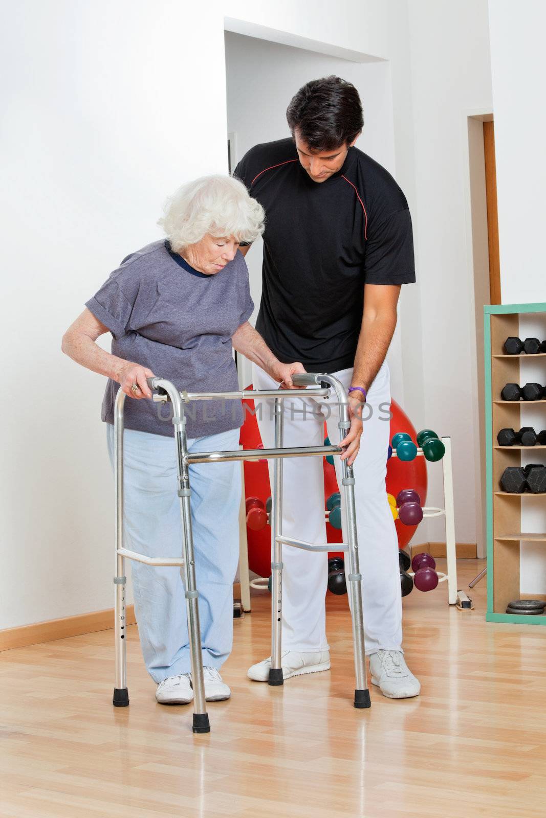 Full length of a trainer assisting senior woman in moving walker