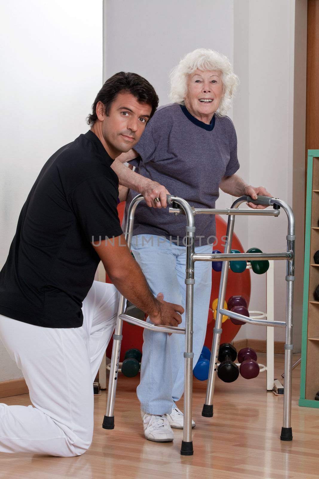 A therapist assisting a senior woman onto her walker.