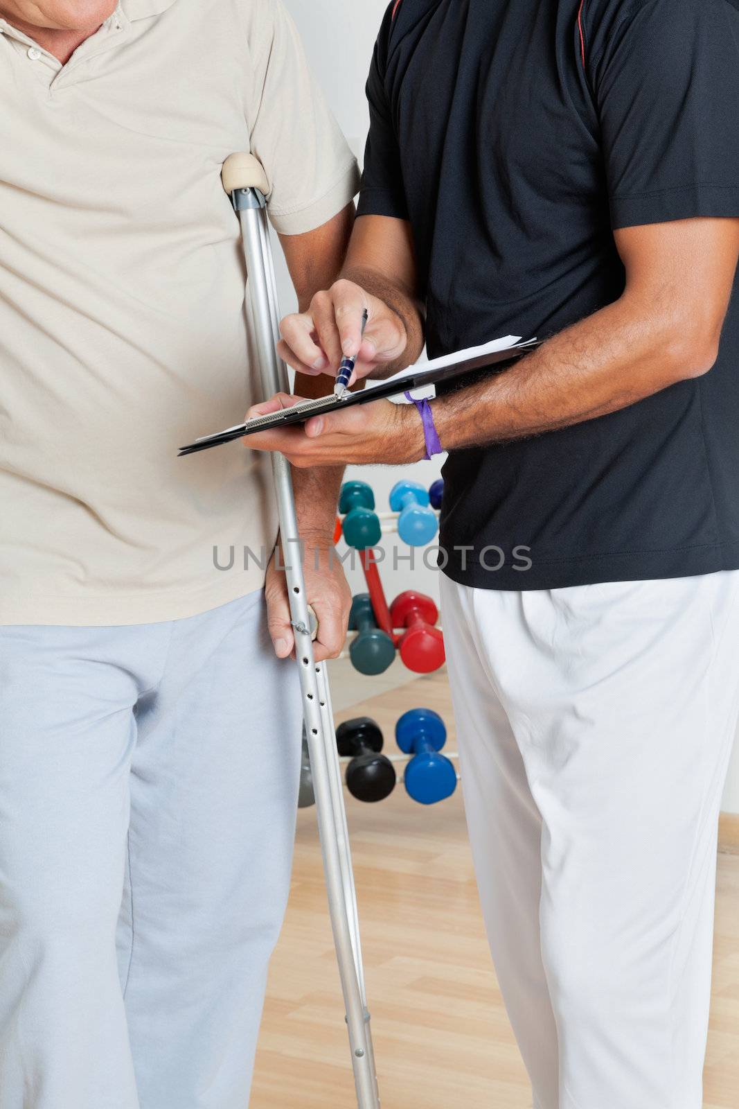 Trainer Holding Clipboard While Standing With Senior Man On Crut by leaf