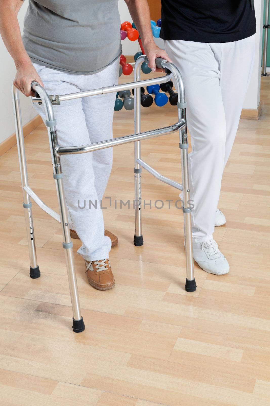 Low section of woman with walker and trainer on wooden floor