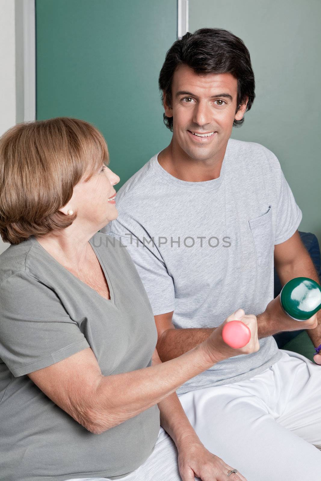 Mature woman exercising in gym with young instructor.
