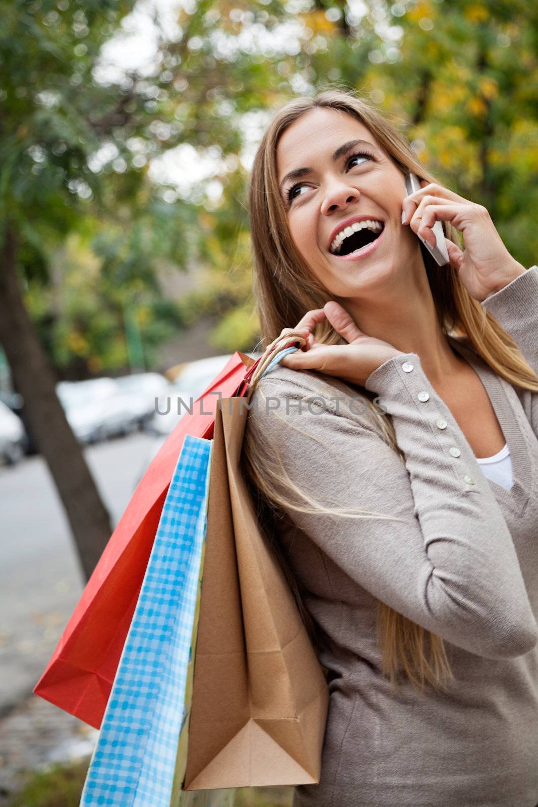 Cheerful young woman communicating on cell phone while carrying shopping bags on shoulder
