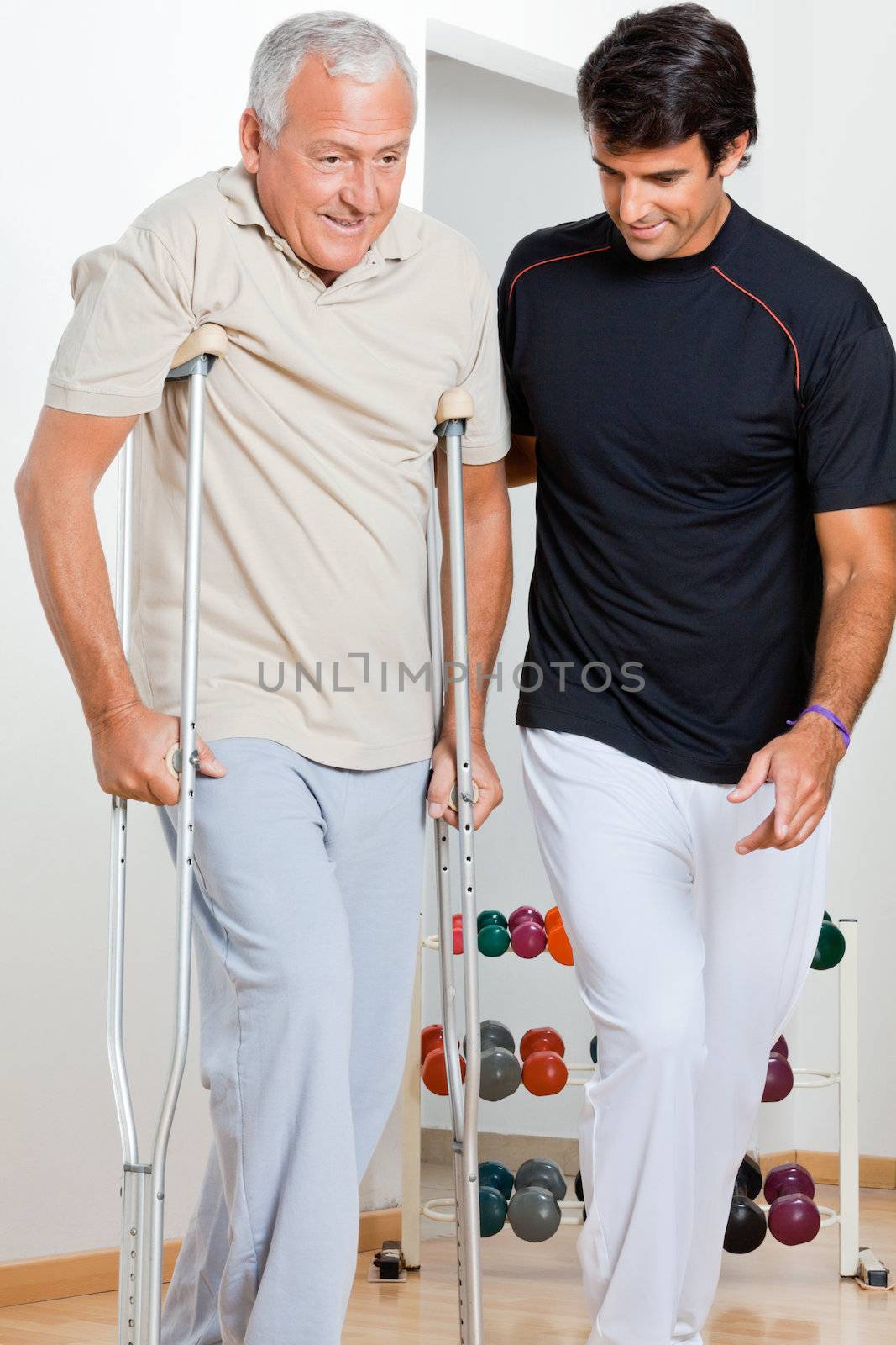 Trainer helping senior man with crutches to walk