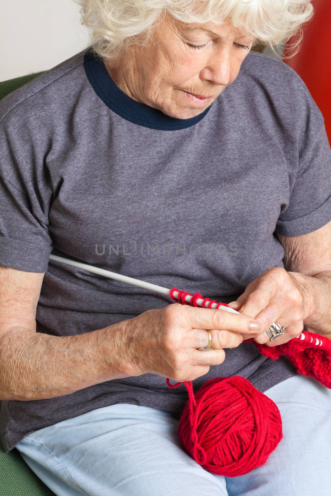 Senior woman using knitting needles with red wool