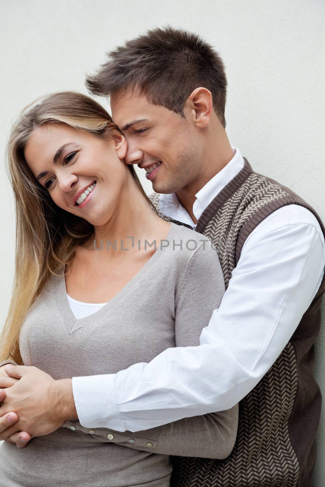 Young man embracing a beautiful woman from behind over colored background