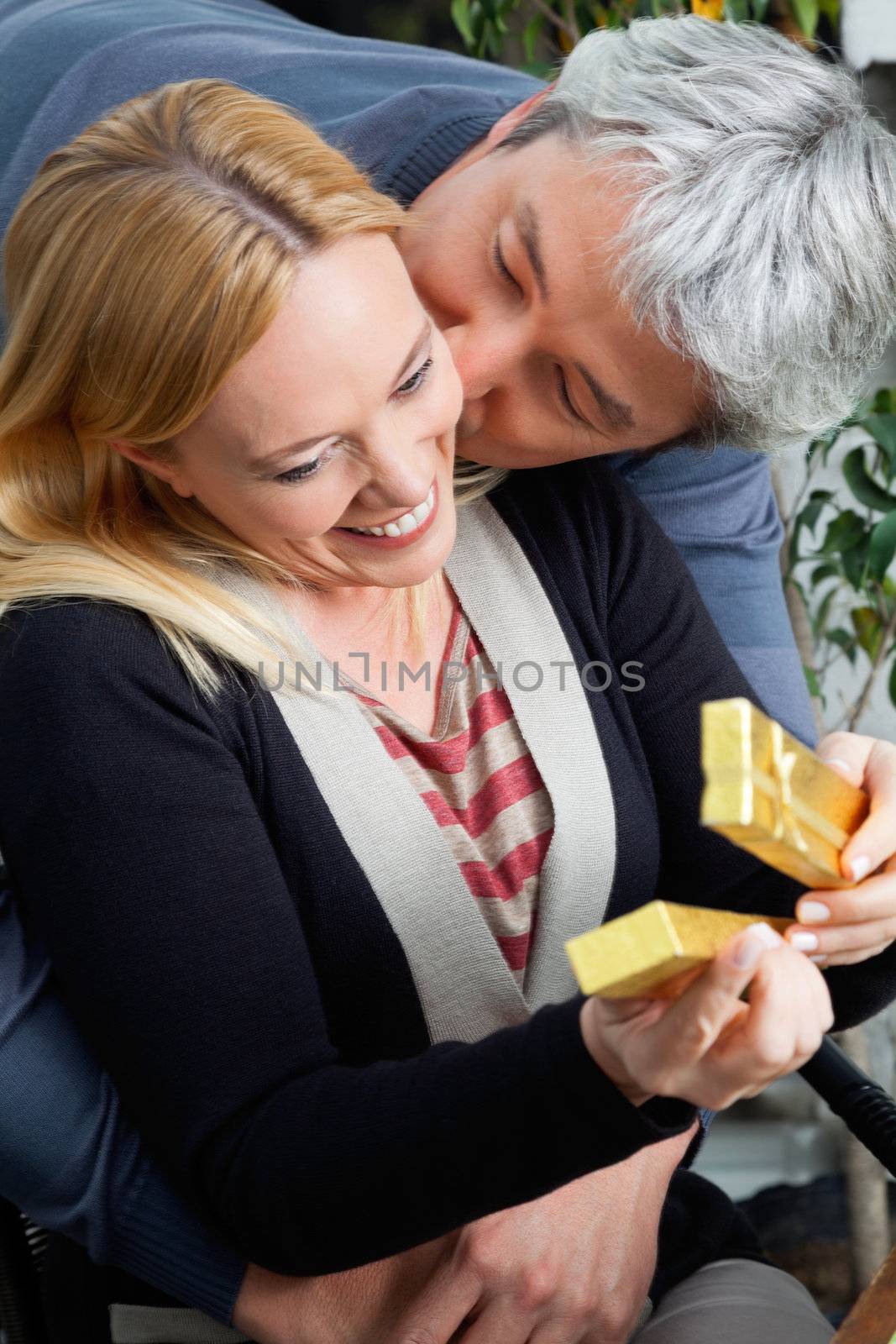 Affectionate middle aged man kissing woman as she opens present