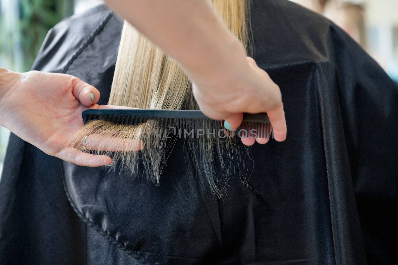 Hairstylist combing hair of a blonde female customer before haircut at salon