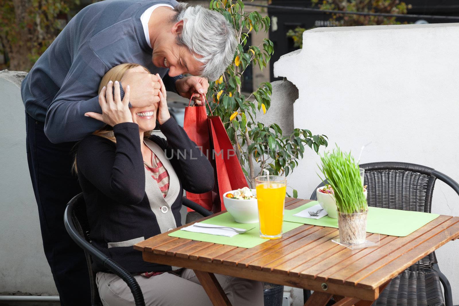 Middle aged man covering woman's eyes on breakfast table for surprise gift