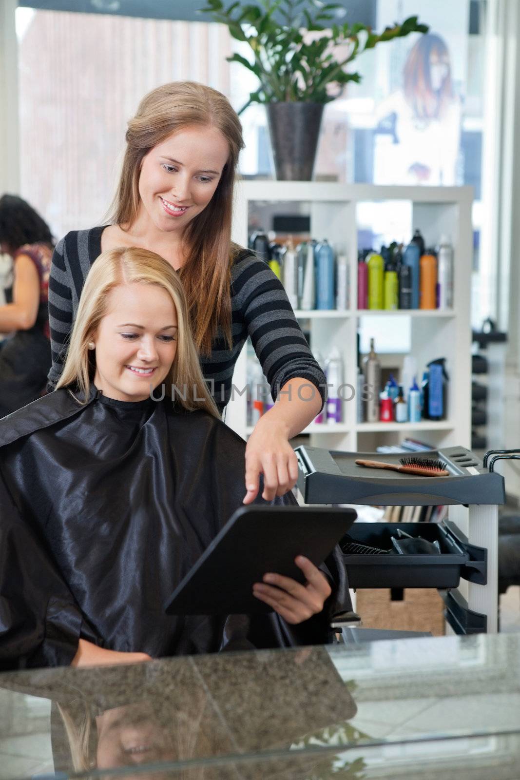 Mirror reflection of hairdresser pointing at digital tablet while female customer holding it