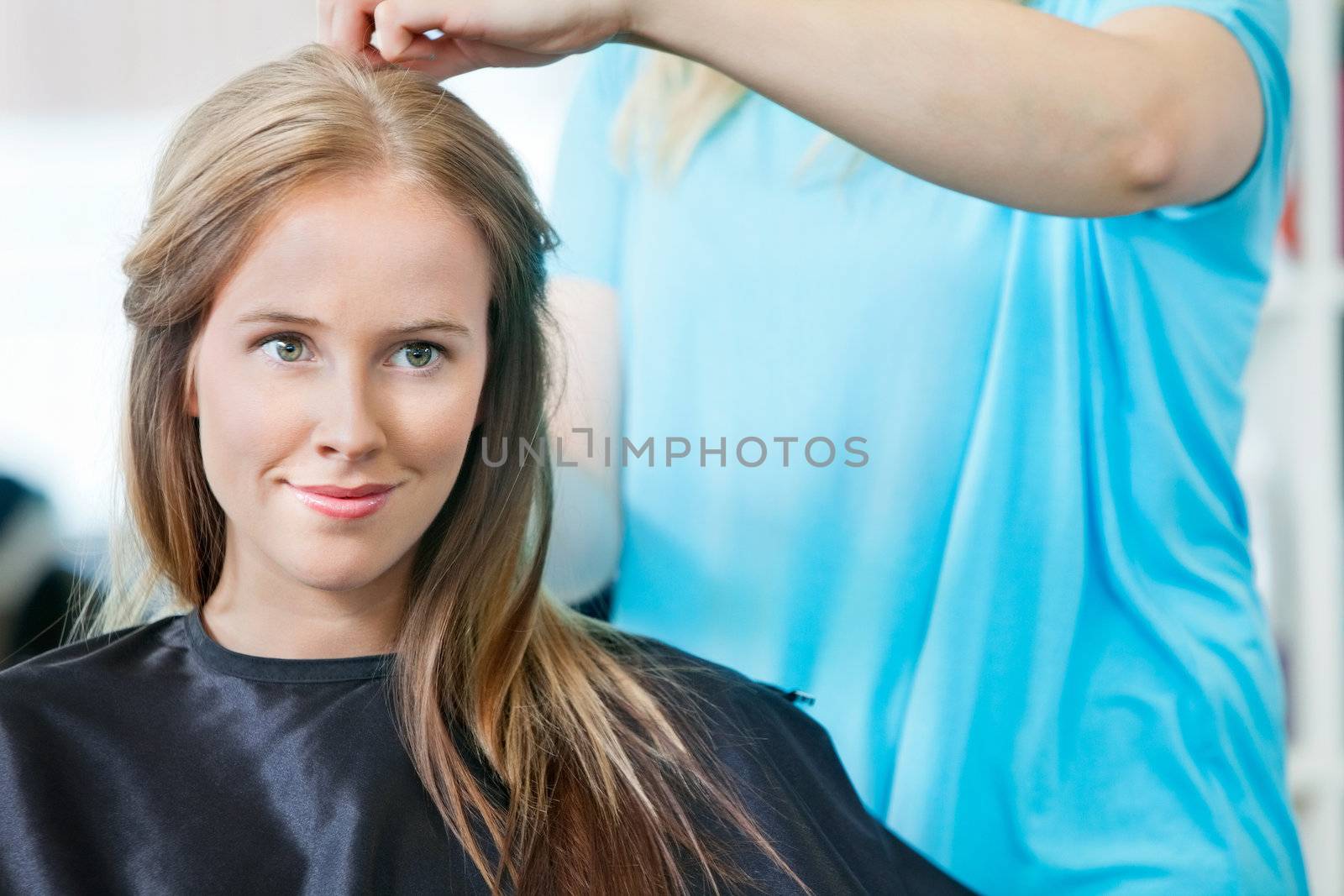 Young woman smiling while hairdresser getting her ready for haircut at parlor