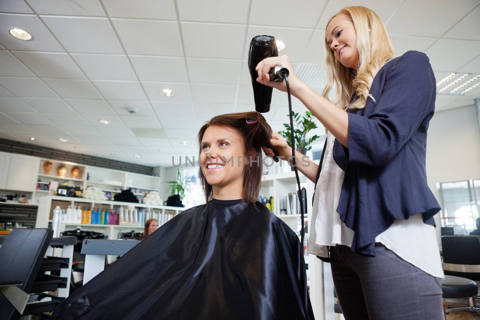 Young beautician blow drying hair of customer after a haircut