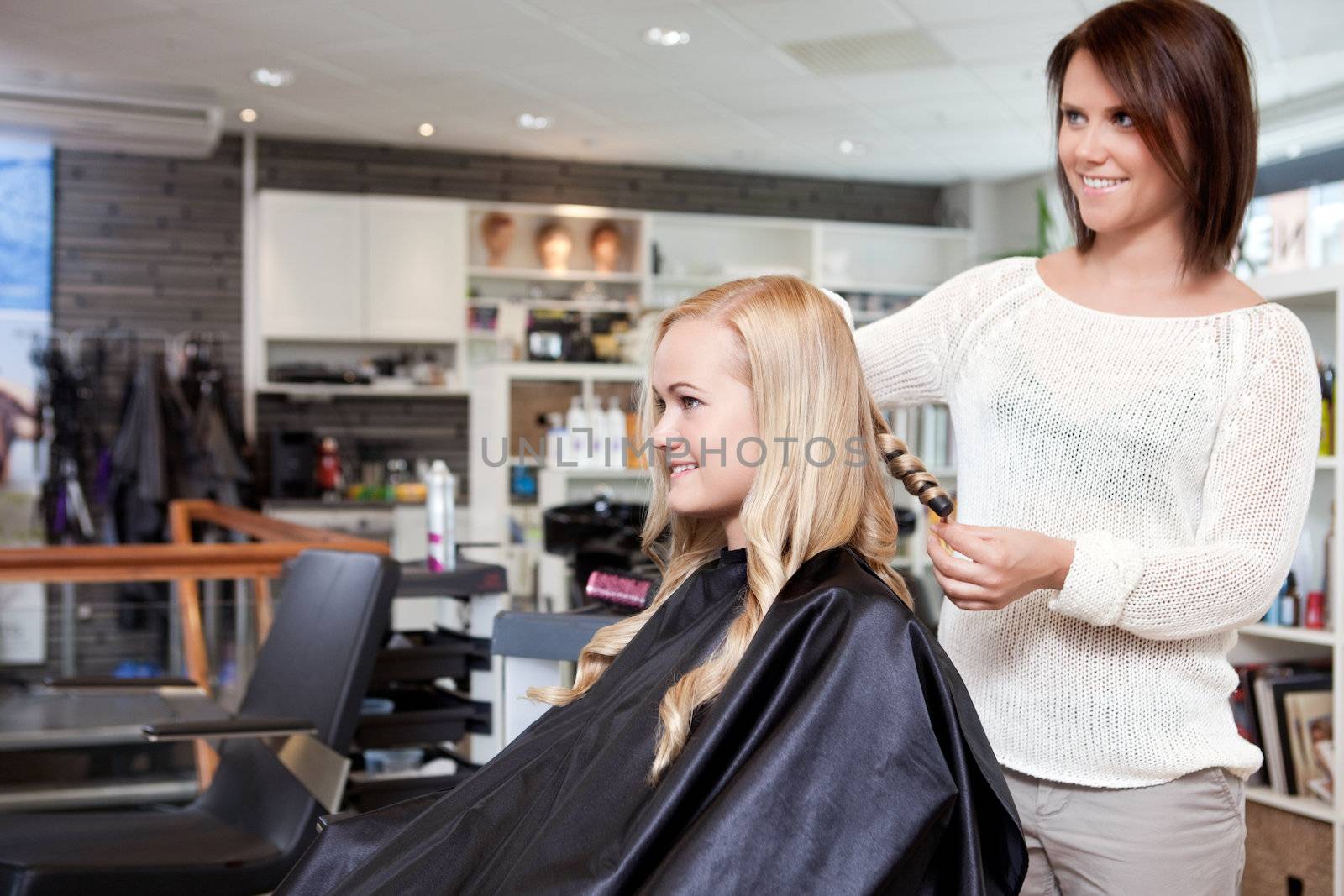 Stylist curling womans hair in beauty salon .