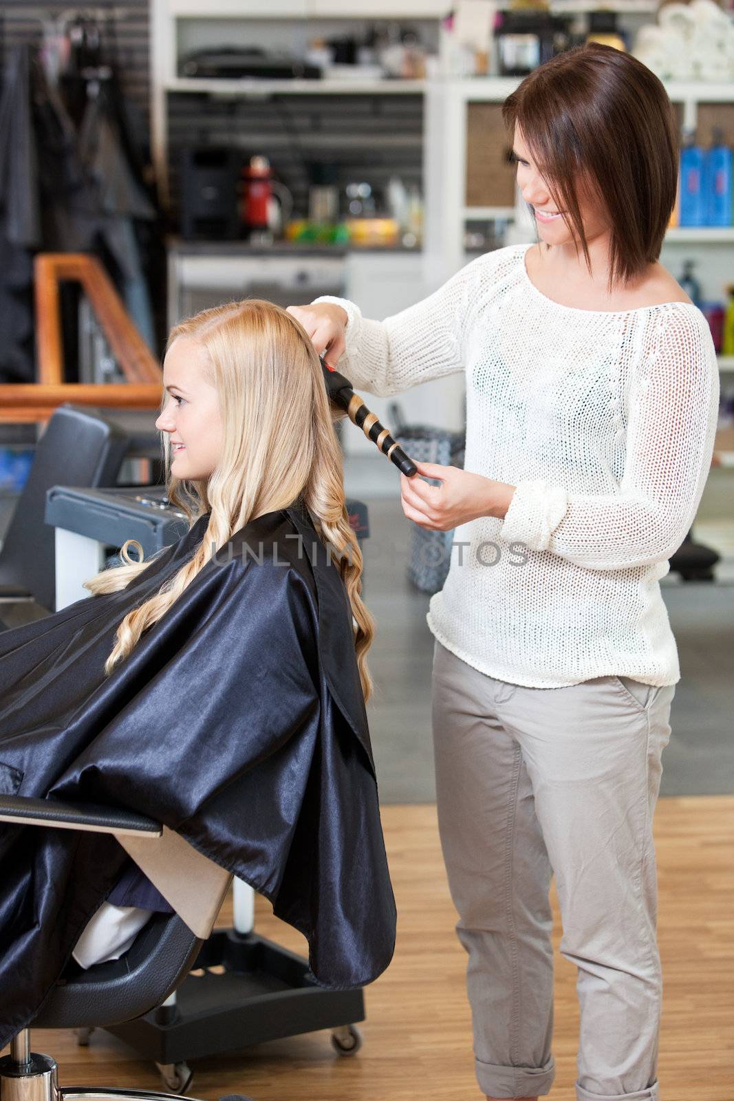 Stylist curling hair of a young blond customer