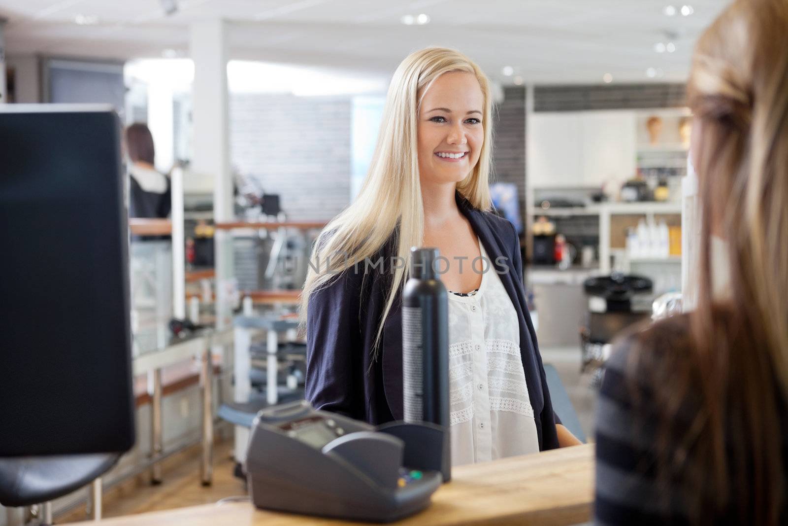 Young blonde woman standing by cash counter at hair salon