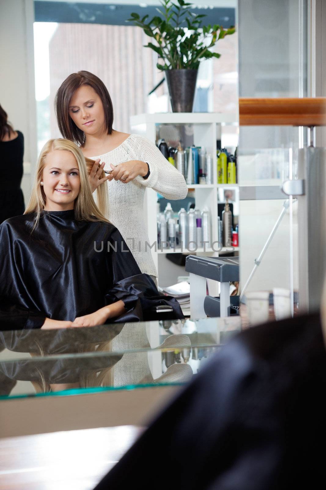 Mirror reflection of hairdresser giving young woman a new haircut at parlor