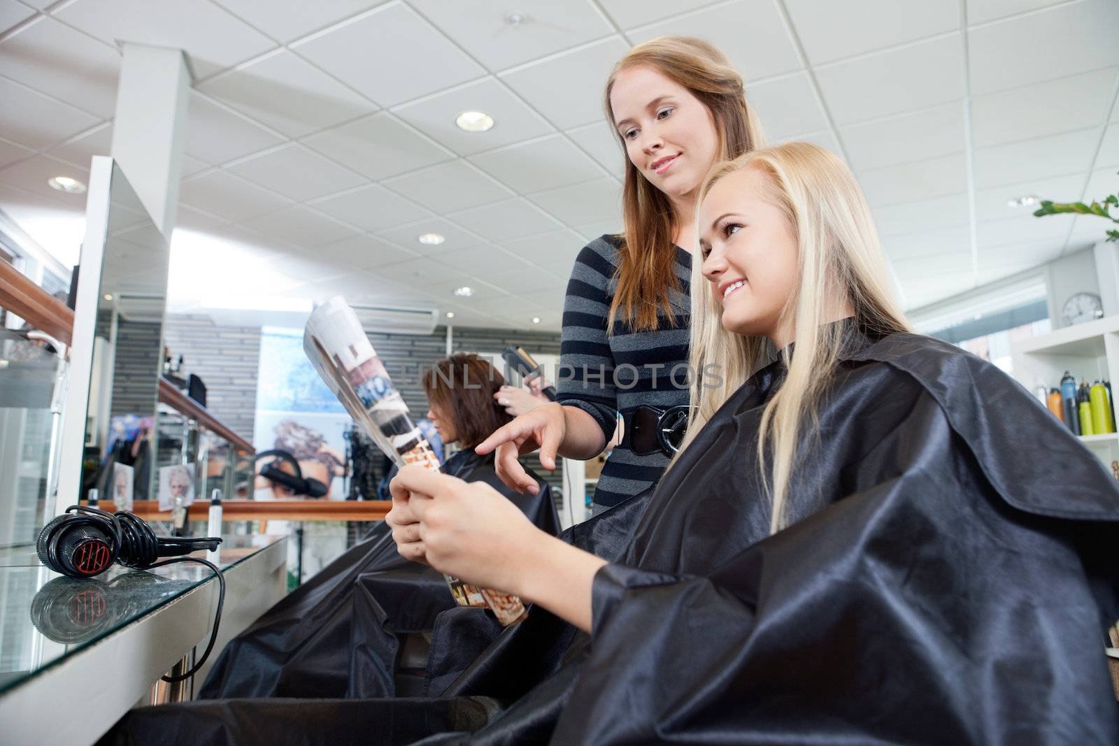 Hairdresser pointing at magazine held by female customer in parlor
