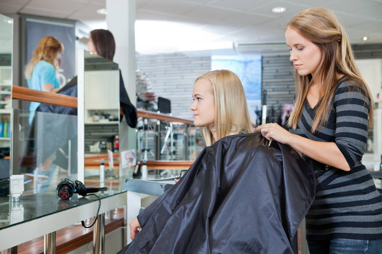 Young hairdresser making preparation before giving a haircut to female customer at parlor