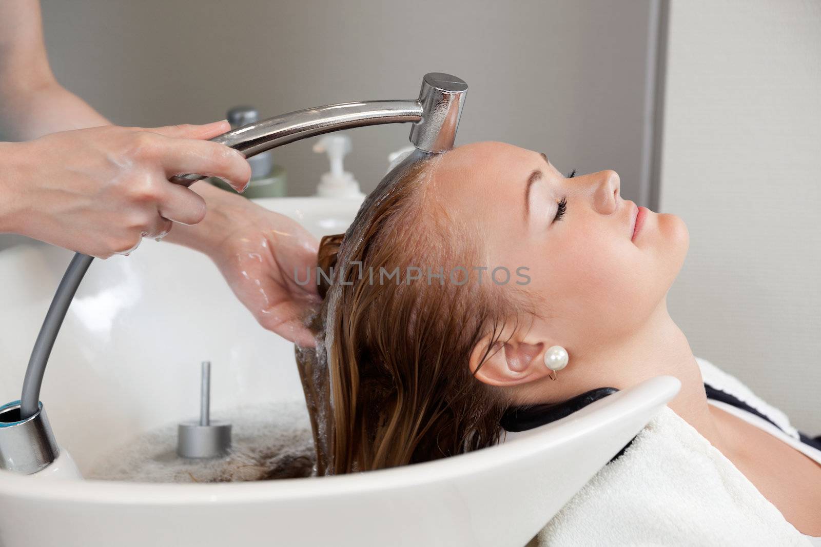 Side view of a beautiful young woman getting a hair washed by hairdresser at salon