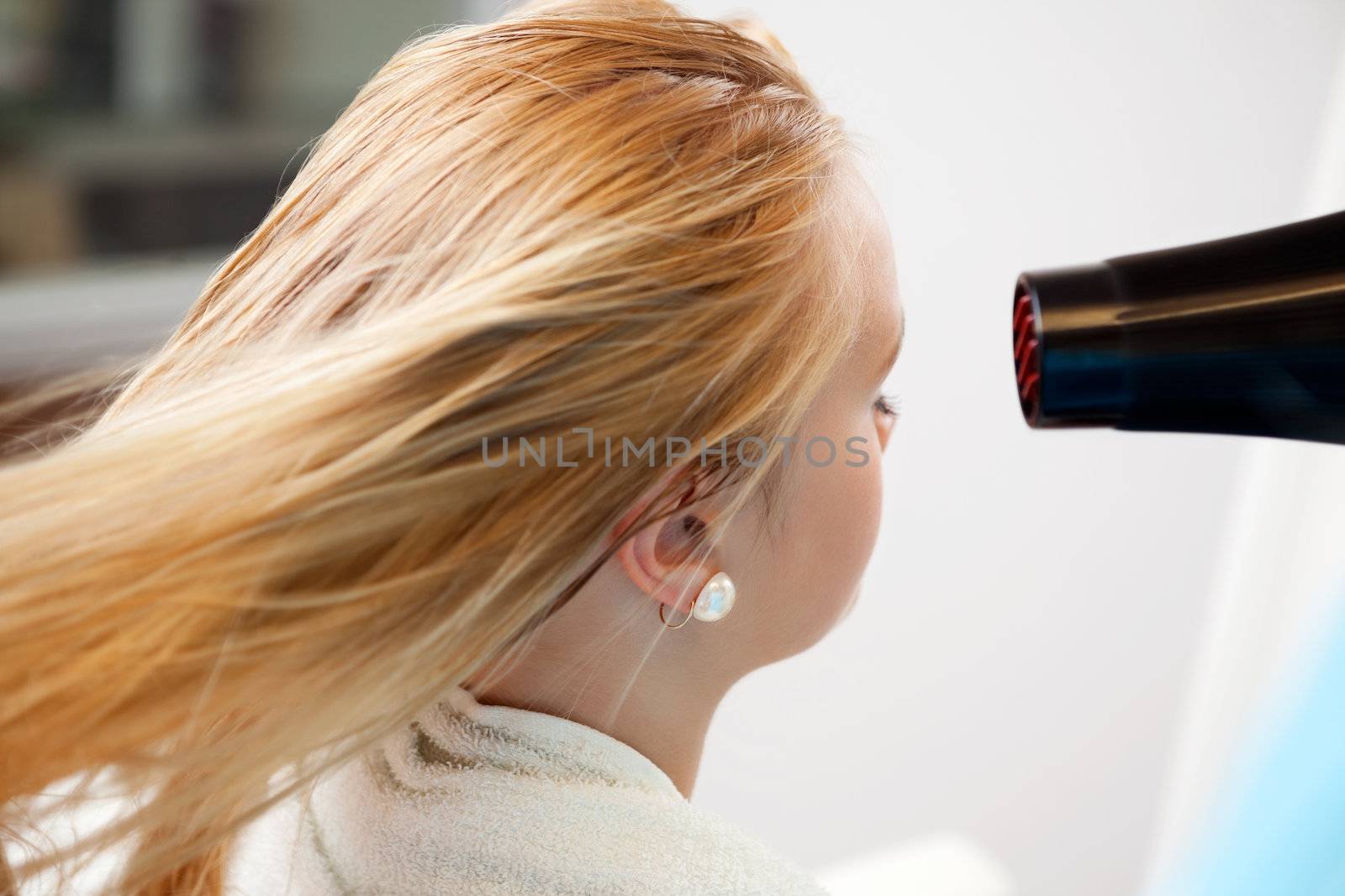Blond hair of a young woman being dried by blow dryer at parlor