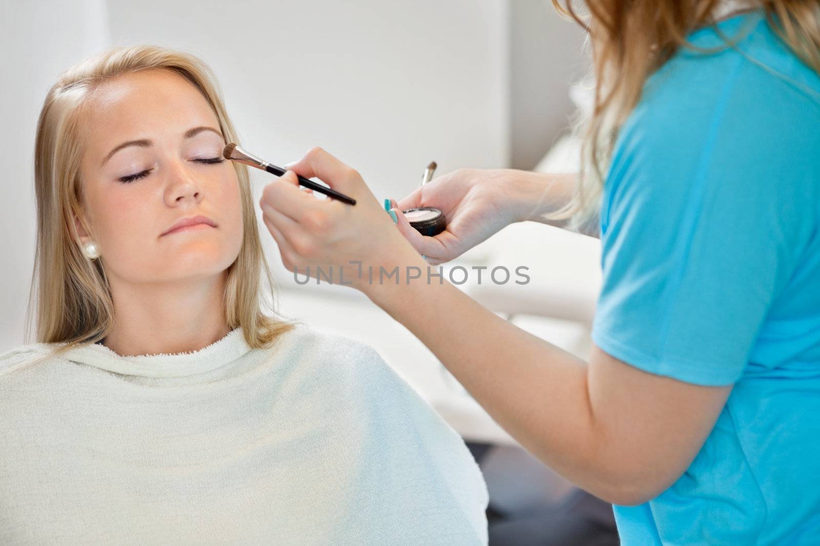 Midsection of beautician applying eye shadow to young woman at parlor
