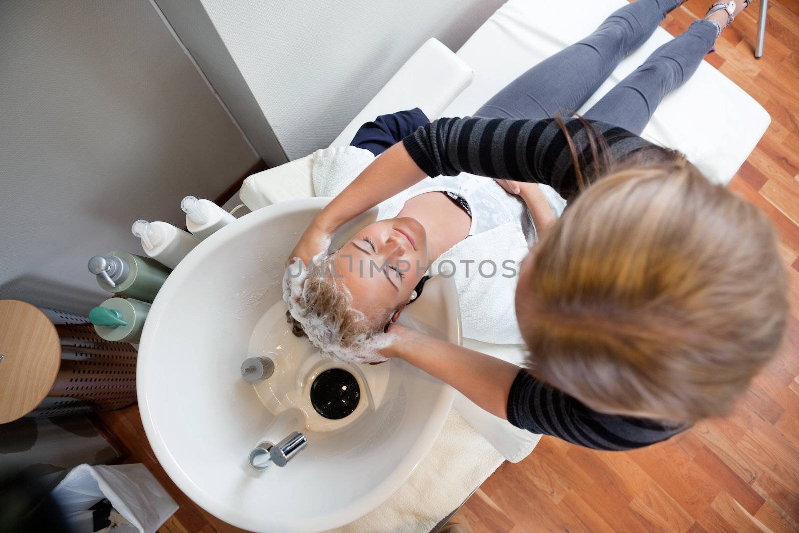 High angle view of female beautician washing customer's hair with shampoo at beauty salon