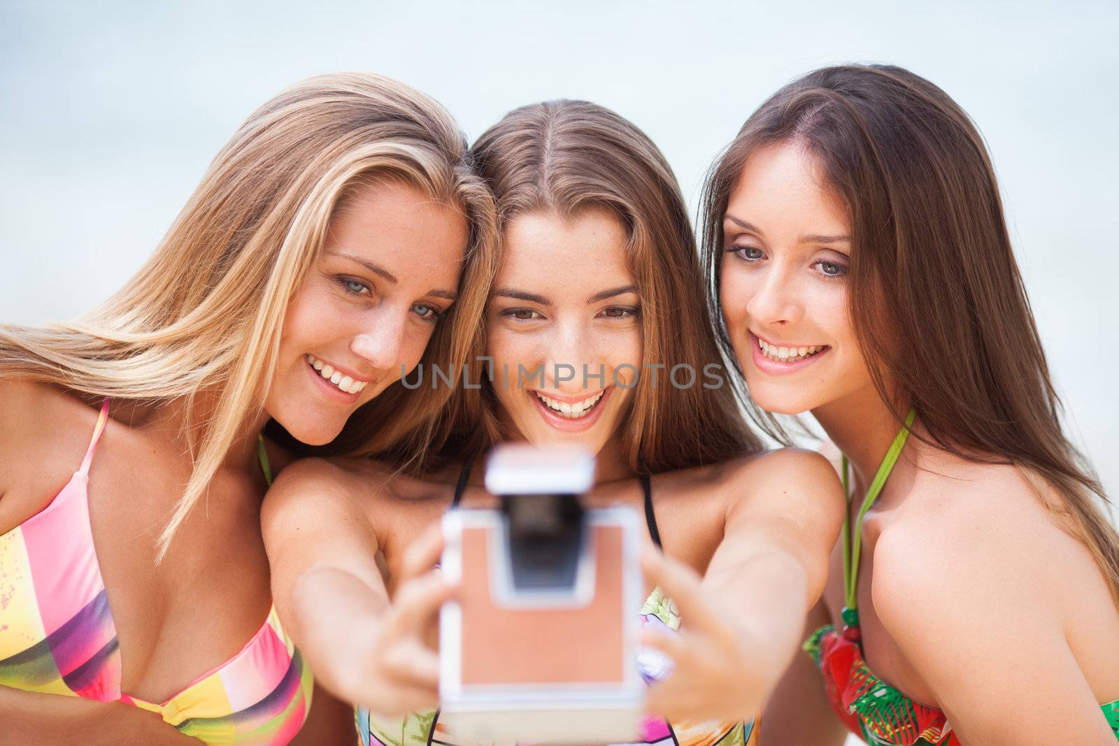 three teenager beautiful girls taking selfie with old camera on the beach