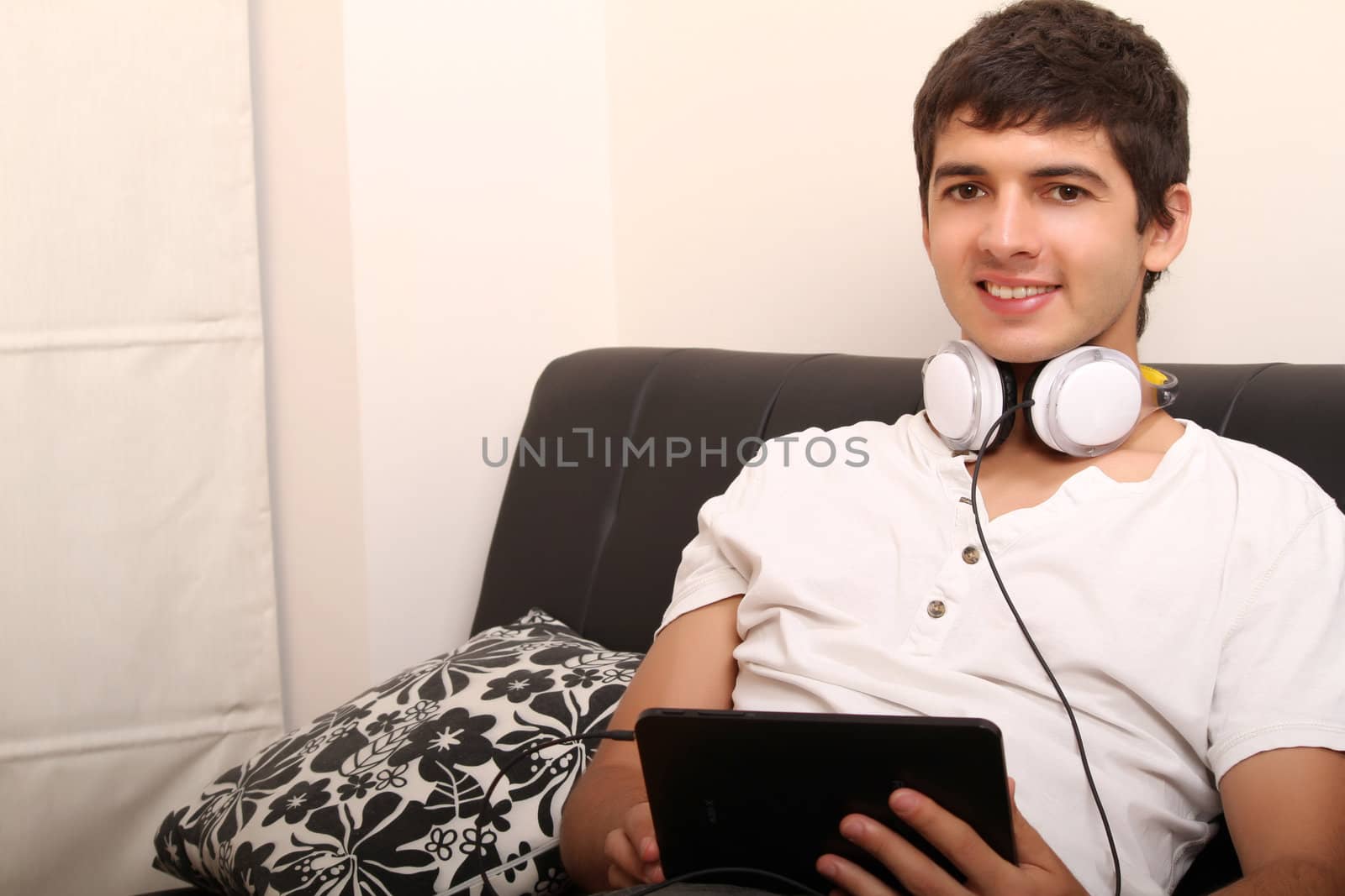 A young, latin man with a Tablet PC and Headphones on the Sofa
