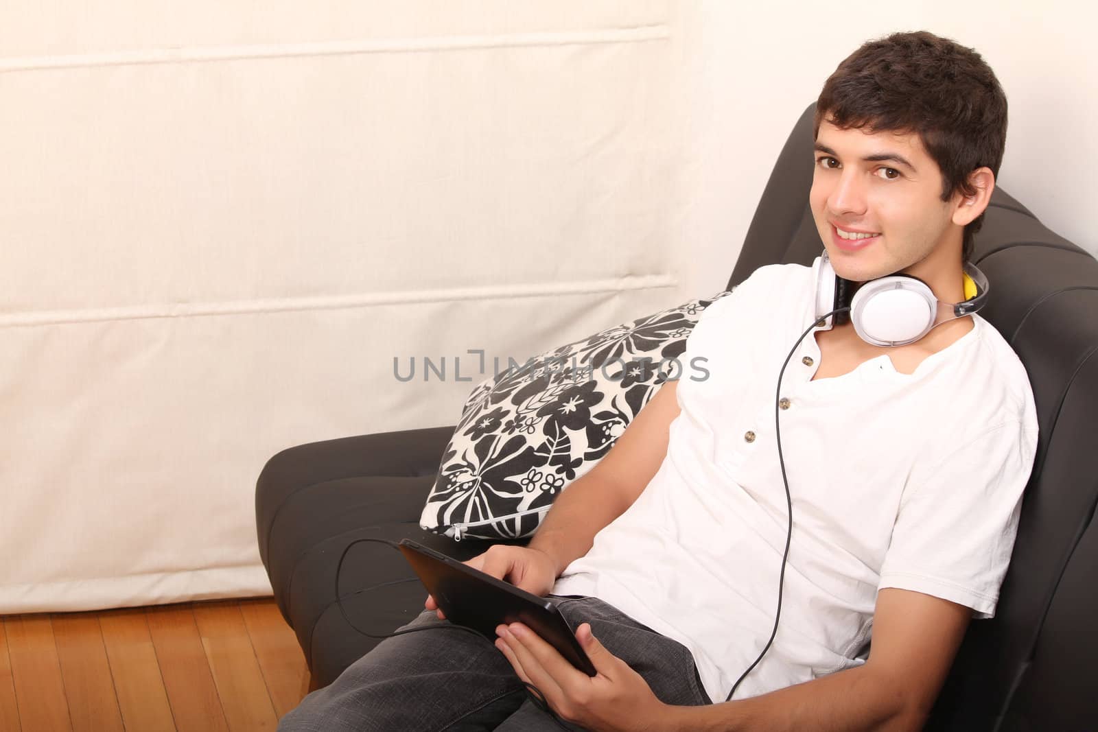 A young, latin man with a Tablet PC and Headphones on the Sofa

