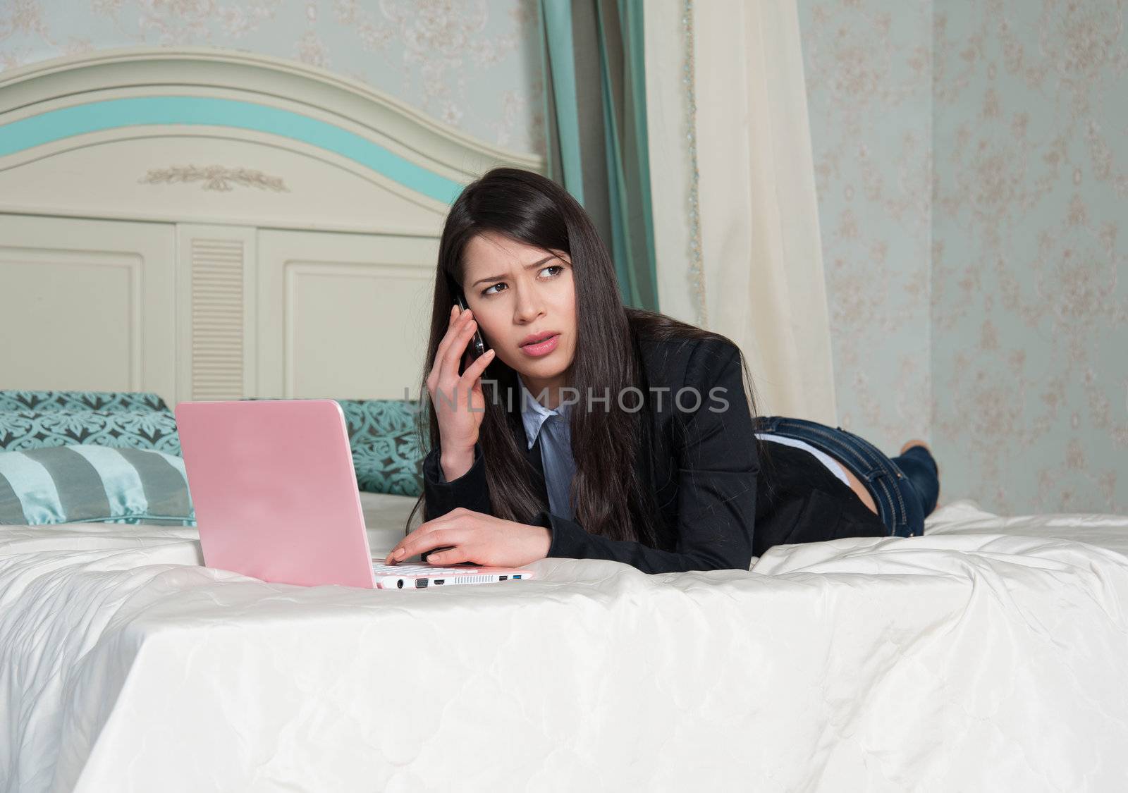 woman lying in bed with your laptop, talking on mobile phone