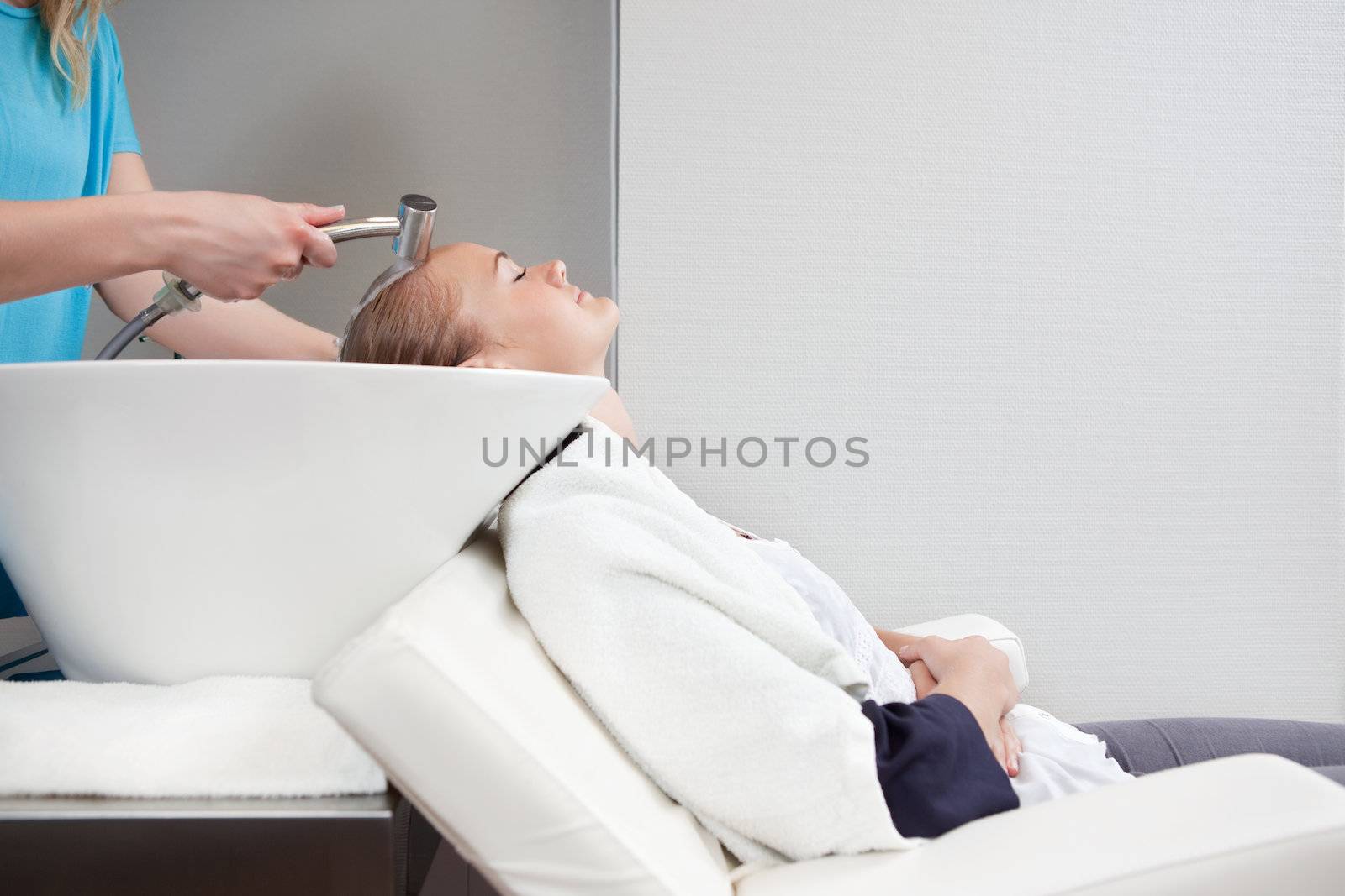 A young blond caucasian woman having her hair washed and rinsed at a beauty salon.