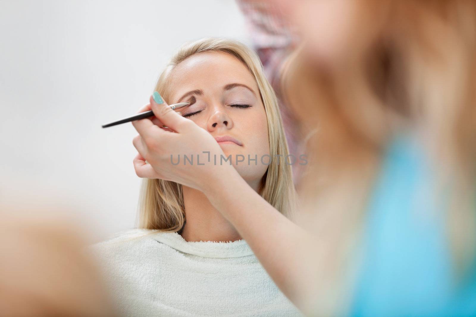 Beautician applying eye shadow to young woman at parlor