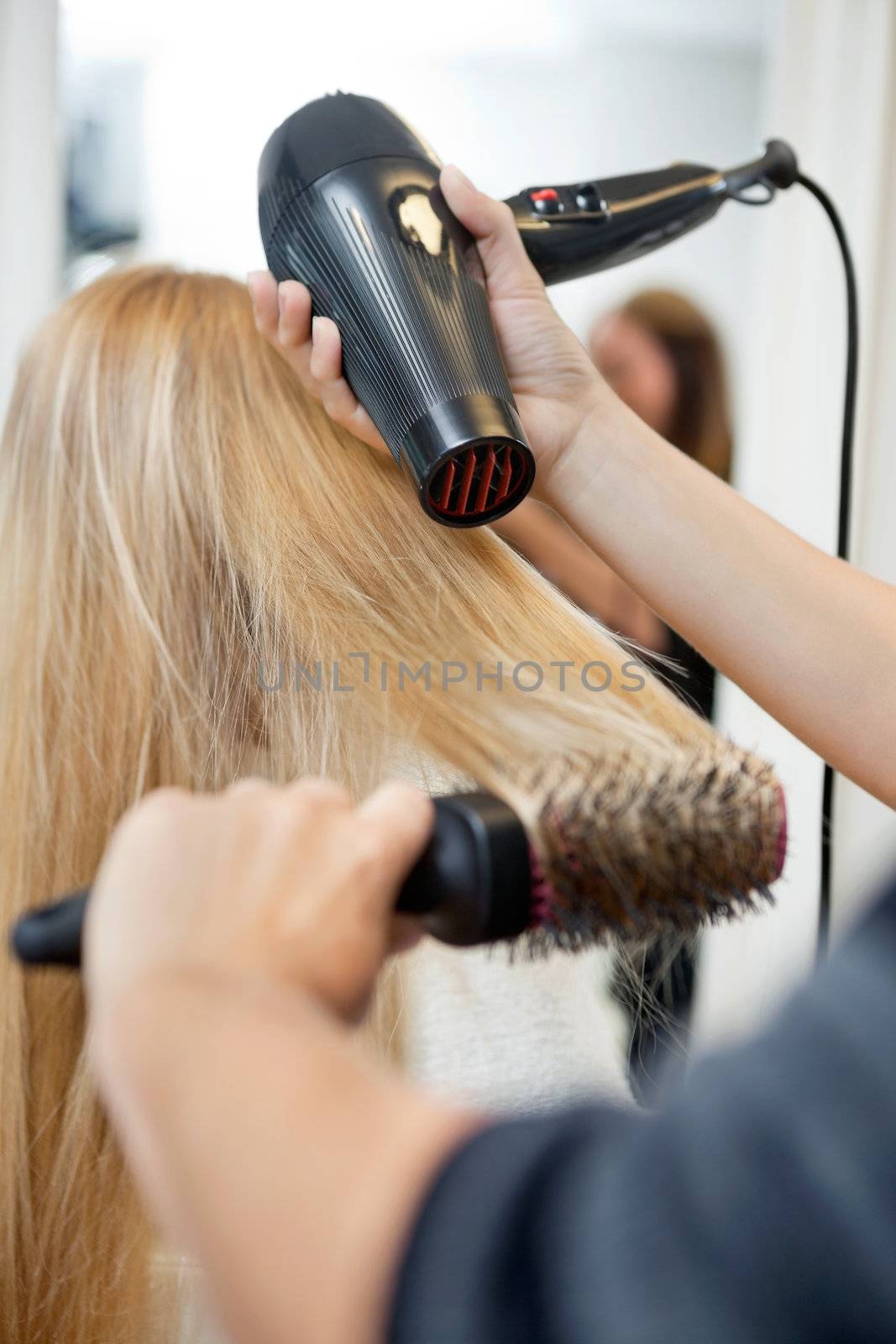 Close up of hairdressers hands drying long blond hair with blow dryer and round brush