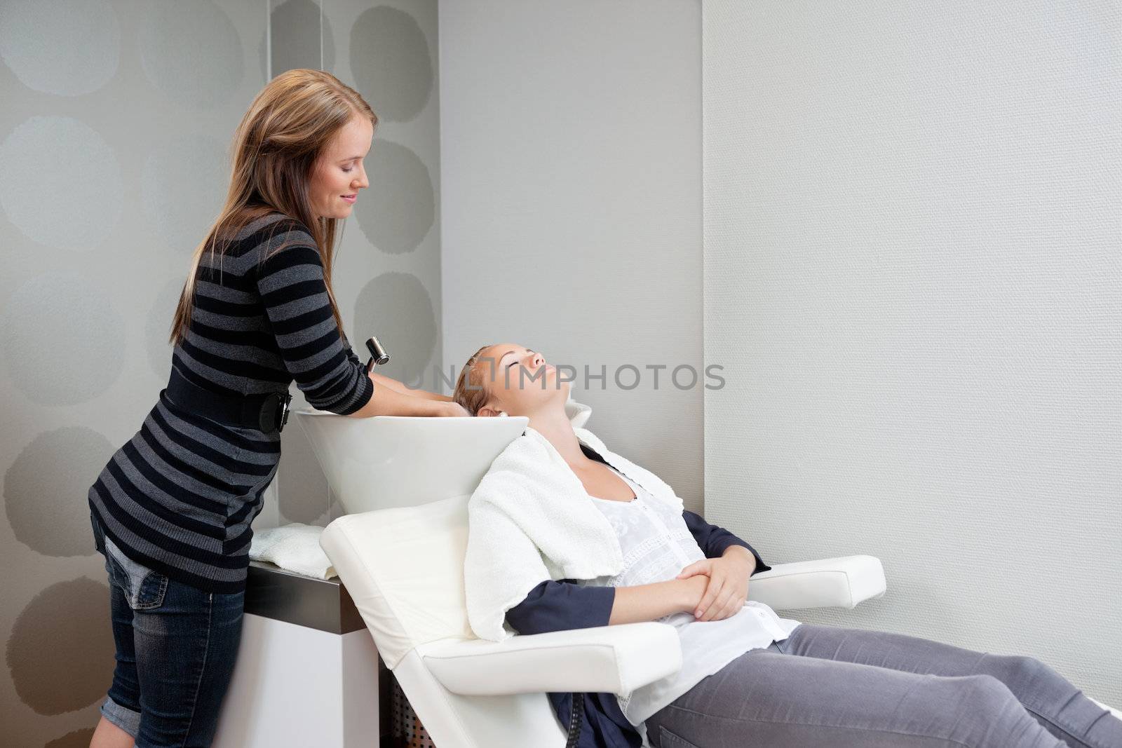 Female beautician washing hair of her customer before haircut at beauty salon
