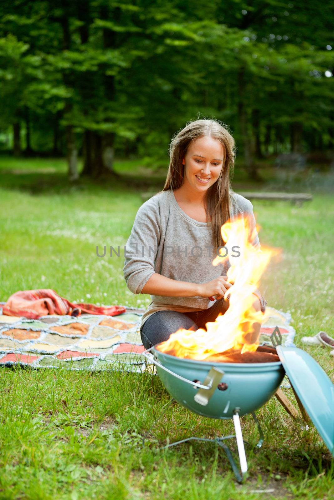 Beautiful young woman sitting in front of flaming portable barbecue at an outdoor picnic