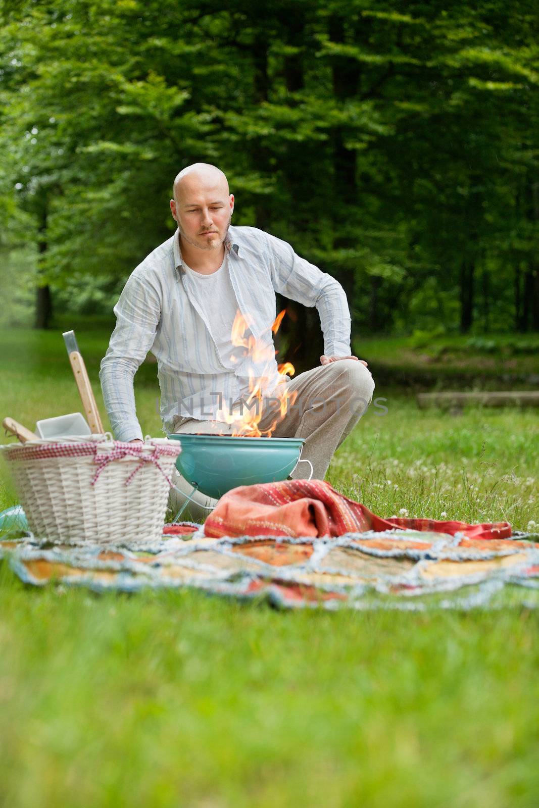 Mature man in casual wear with a flaming portable barbecue at an outdoor picnic
