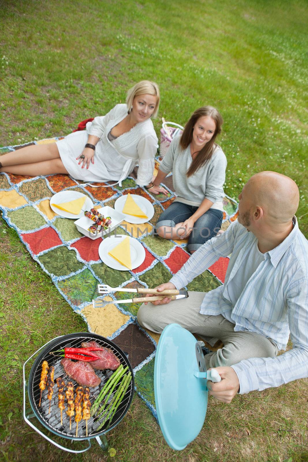 High angle view of man cooking meat on portable barbeque while looking at friends