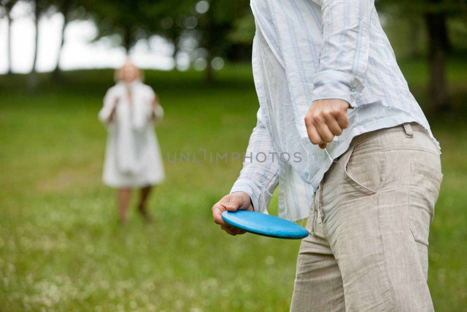 Midsection of man in casual wear ready to throw flying disc with woman in background