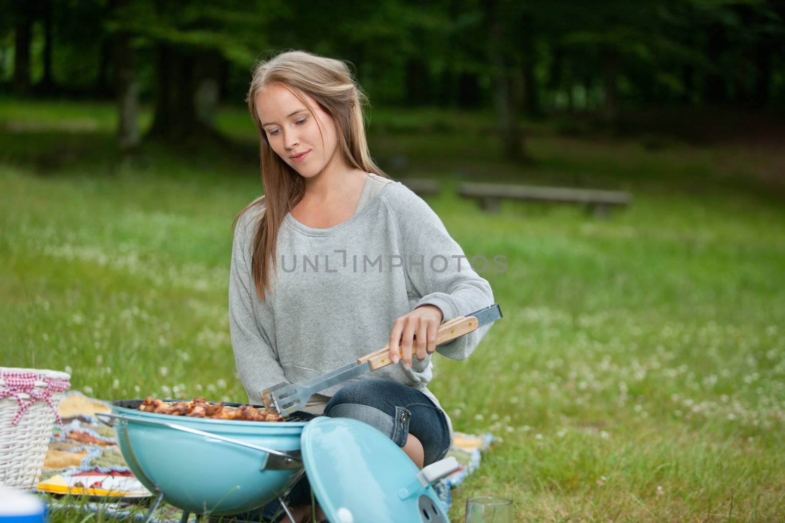Cute young woman in casual wear cooking food on a portable barbecue in park at weekend outing
