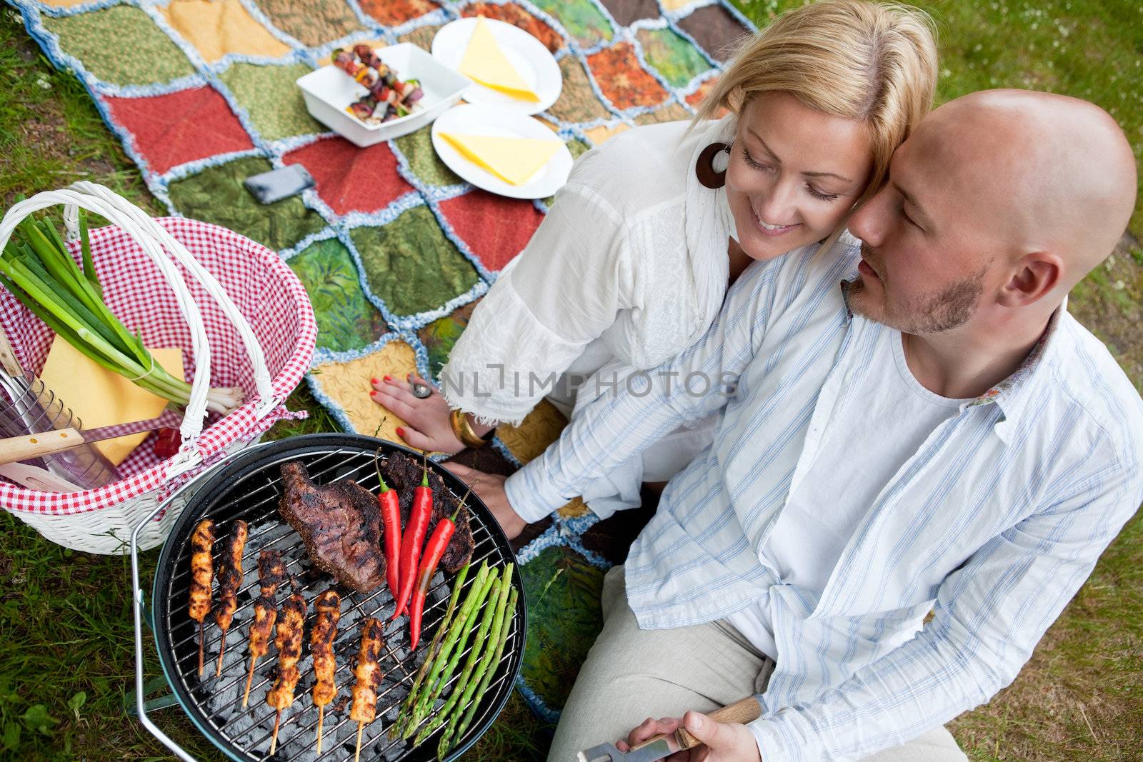 A happy couple sitting close cooking food on a BBQ in the park