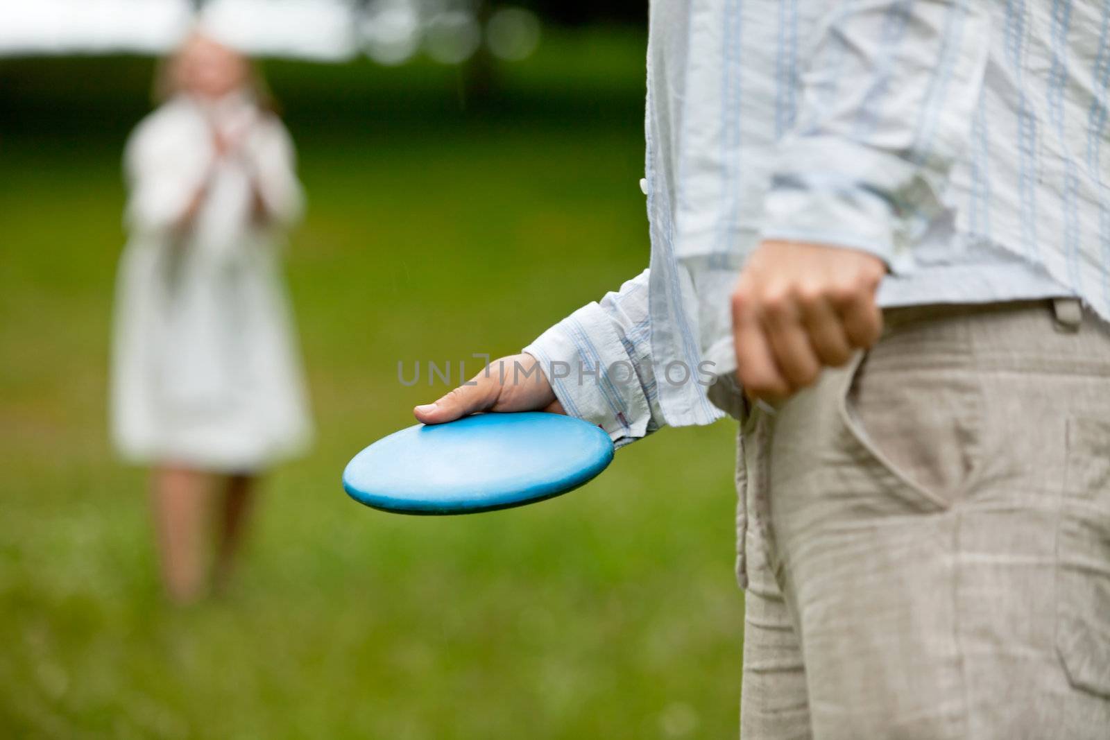 Midsection of man in casual clothing ready to throw Frisbee with woman in background