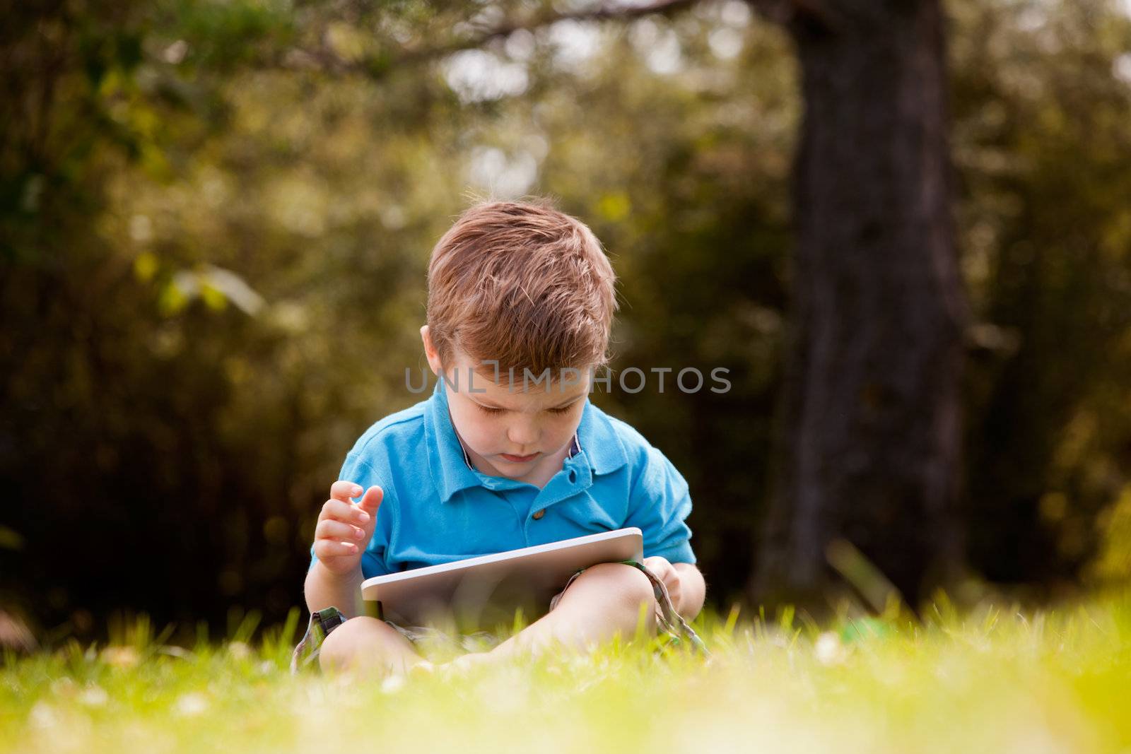 Cute young boy playing with a digital tablet outdoors in park