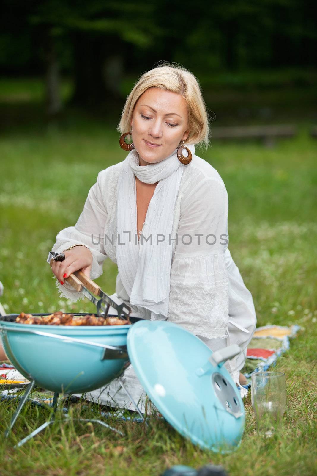 Beautiful mature woman in casual wear cooking food on a portable barbecue on a weekend outing