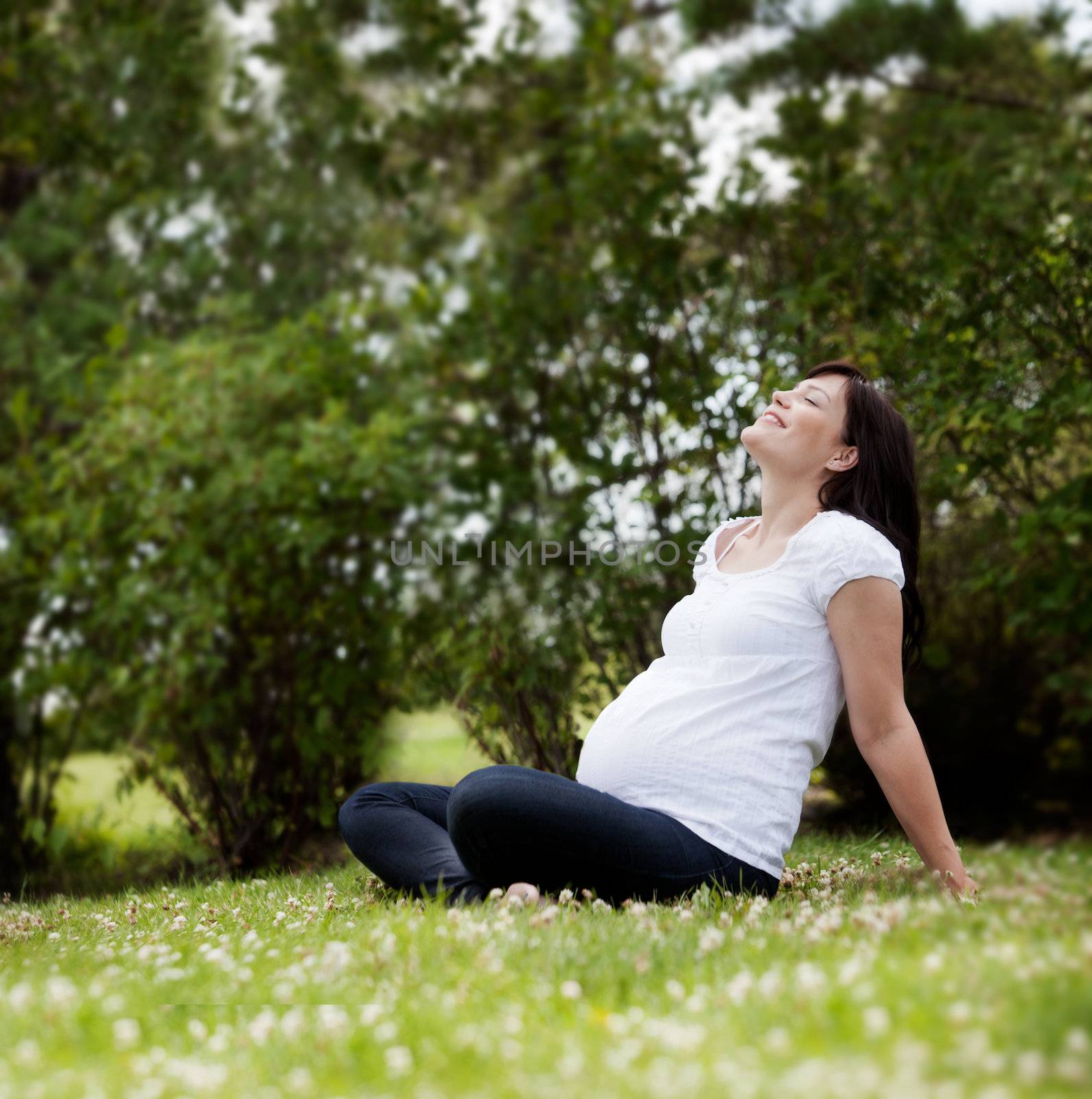 Happy attractive pregnant woman in park leaning back enjoying the sun