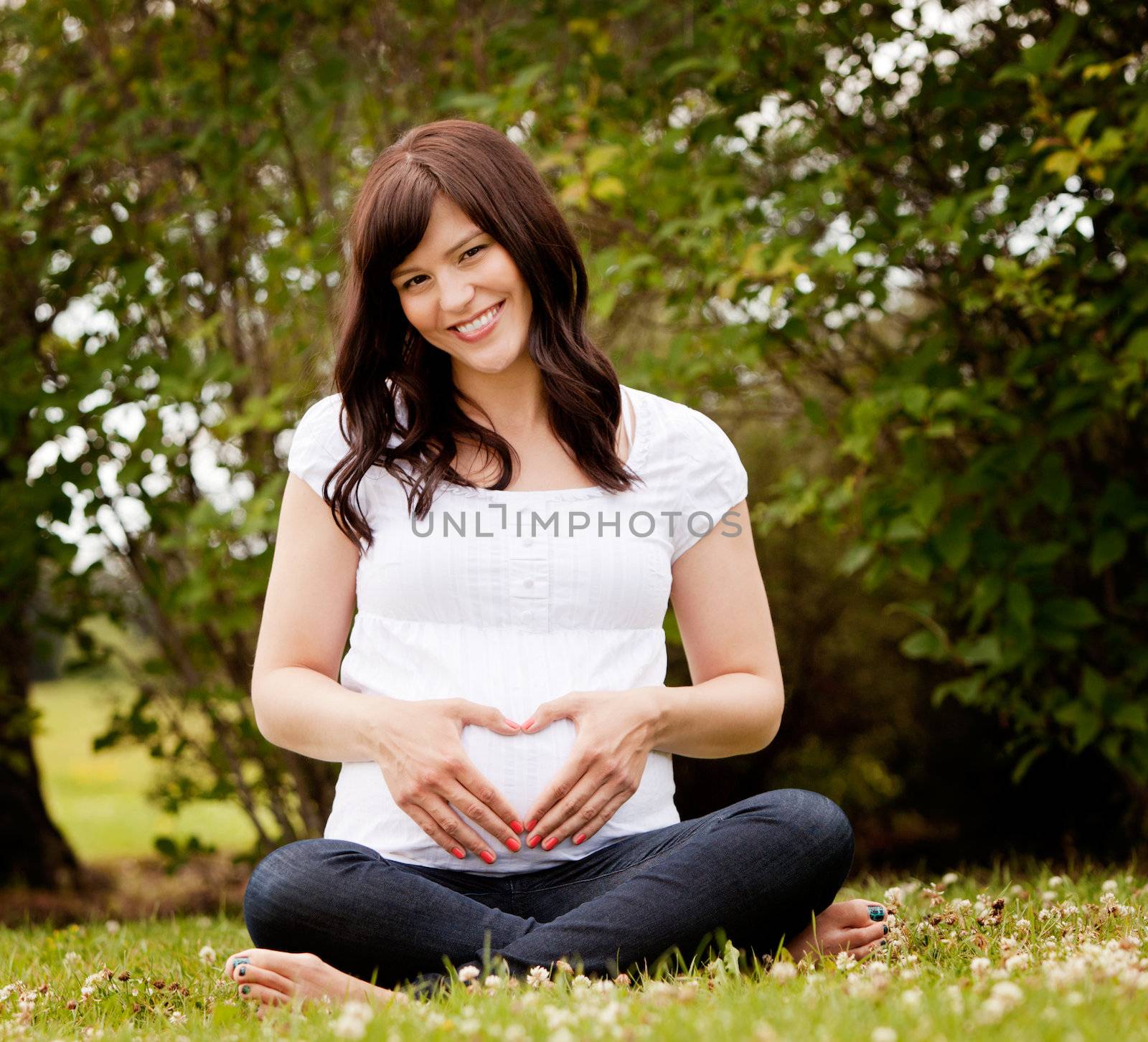 Portrait of a happy healthy pregnant woman in park making heart sign on belly