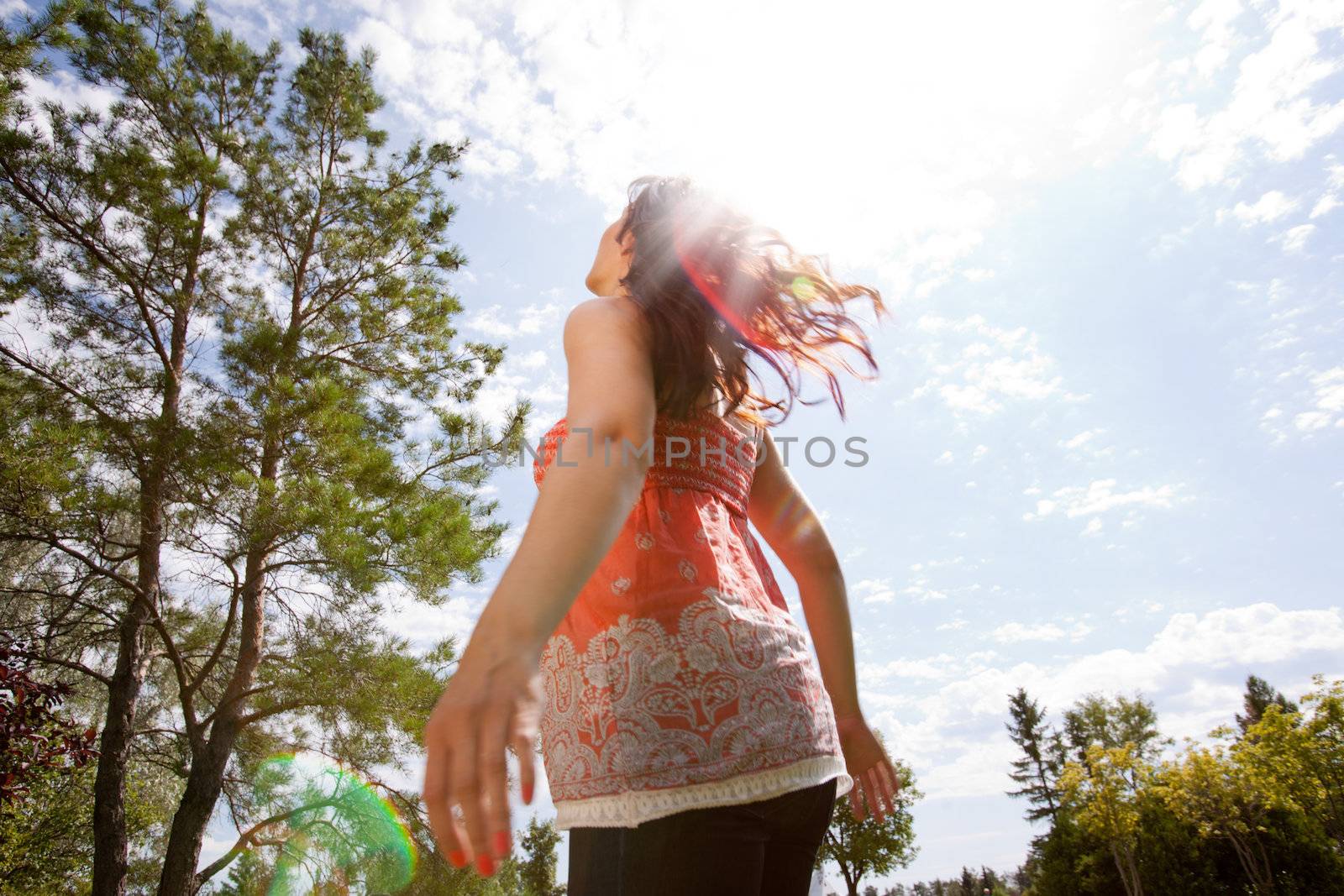 Happy pregnant woman looking to sky with arms back in park